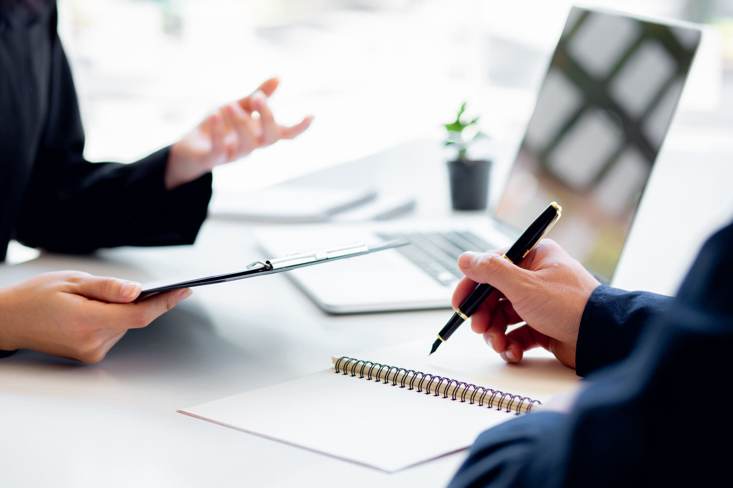 desk with two people, who you can only see their hands, holding pens and  a clipboard